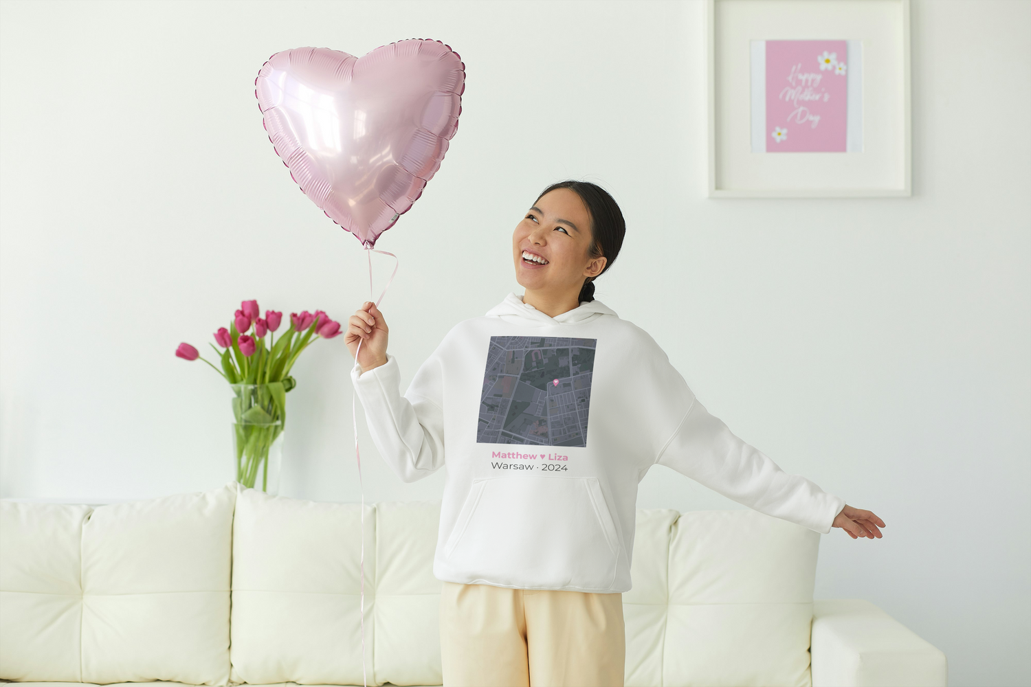 Woman holding a heart-shaped balloon and flowers in a living room. 
